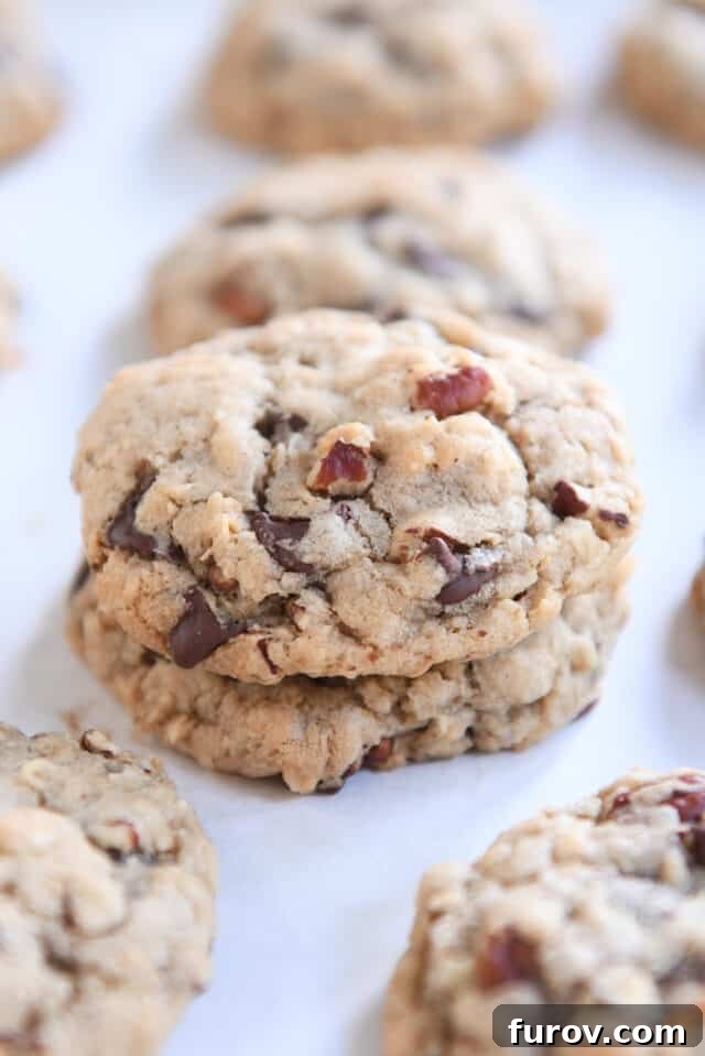 Two golden-brown Cowboy Cookies, perfectly baked and stacked on a pristine white parchment paper, highlighting their inviting texture and rich appearance.