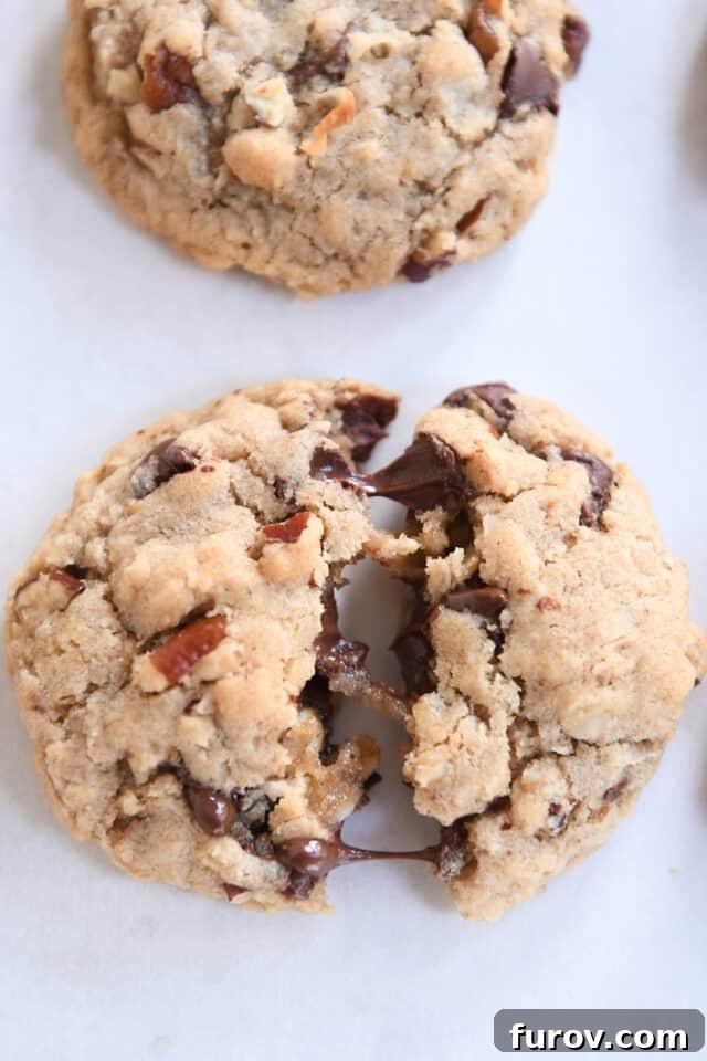 A warm Cowboy Cookie, expertly split in half, showcases the luscious, melted chocolate chips oozing within its soft, inviting interior.