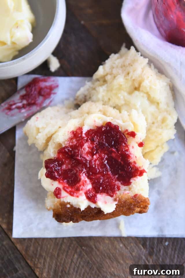 A half of a golden-brown Butter Swim Biscuit, topped generously with creamy butter and vibrant raspberry jam, showcasing its fluffy interior.