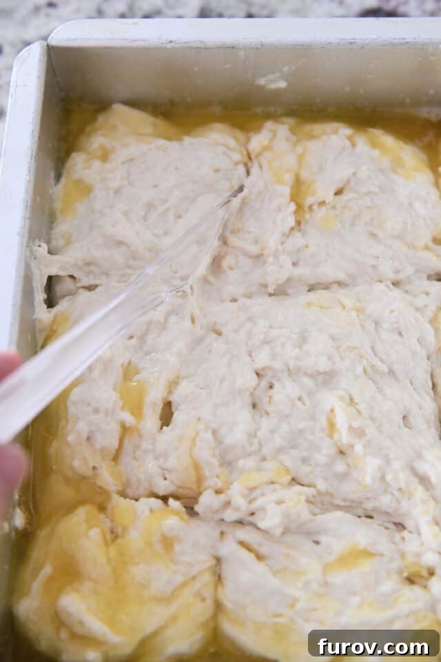 A plastic knife making clean scores through the thick biscuit dough, which is already sitting in a pool of melted butter in a baking pan, preparing it for baking.