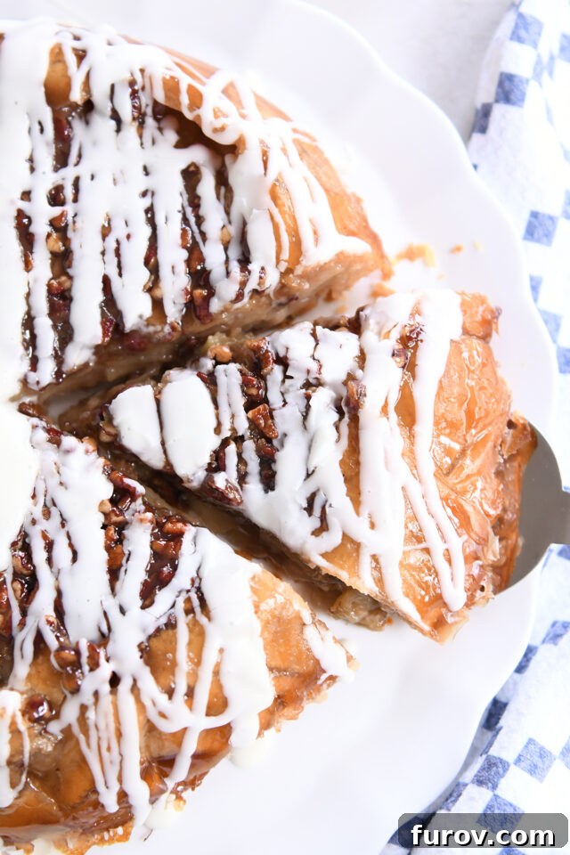 Slice of apple pie on white platter with pecans and glaze on top.
