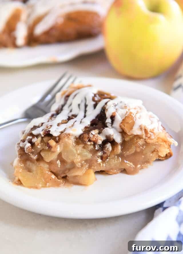 Slice of apple pie on white plate with pecans and glaze on top.