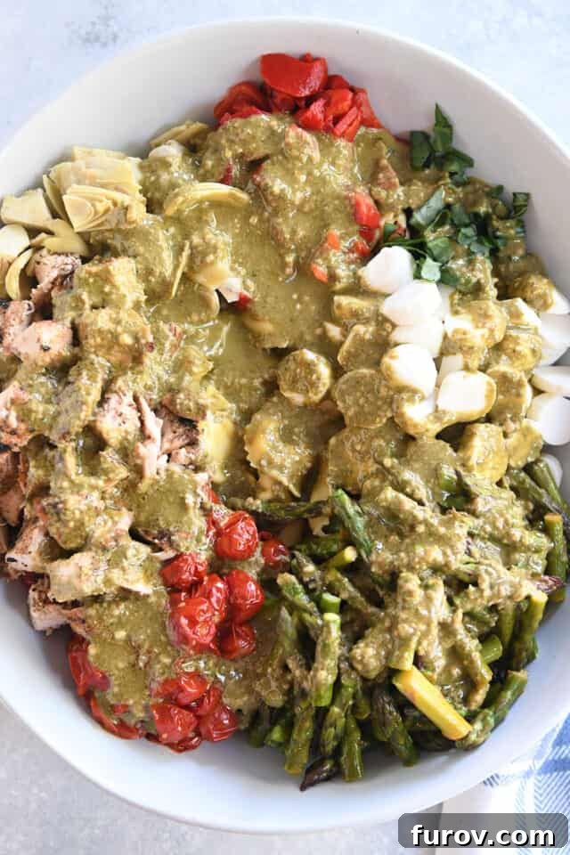 Tangy Pesto Balsamic Chicken Tortellini Medley 6 Rich pesto dressing generously coats the vibrant salad ingredients in a large white bowl, ready for tossing.