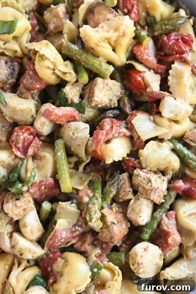 Tangy Pesto Balsamic Chicken Tortellini Medley 7 Close-up of a vibrant salad featuring roasted asparagus, plump tortellini, sweet roasted tomatoes, savory red peppers, and succulent grilled chicken, all perfectly tossed together.