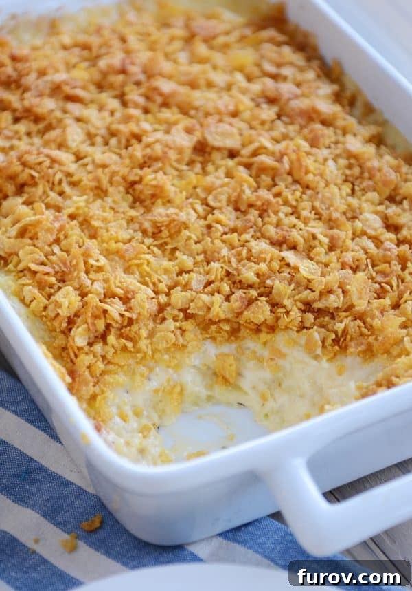 Pan of cheesy funeral potatoes with scoop taken out, showcasing the golden cornflake topping and creamy interior.