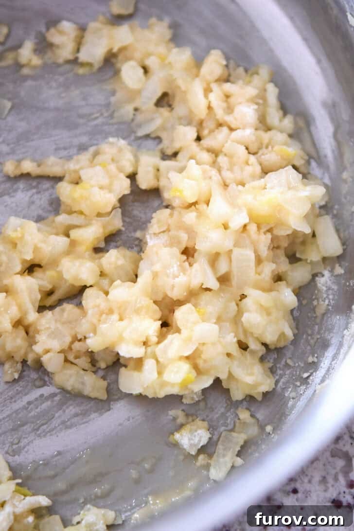 Top-down view of translucent sautéed onions glistening in melted butter within a cooking pot.