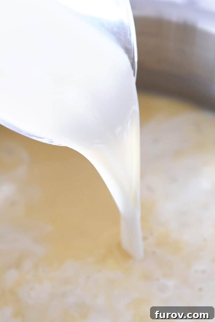 Fresh milk being poured into a creamy white sauce base, creating a swirl of liquid.