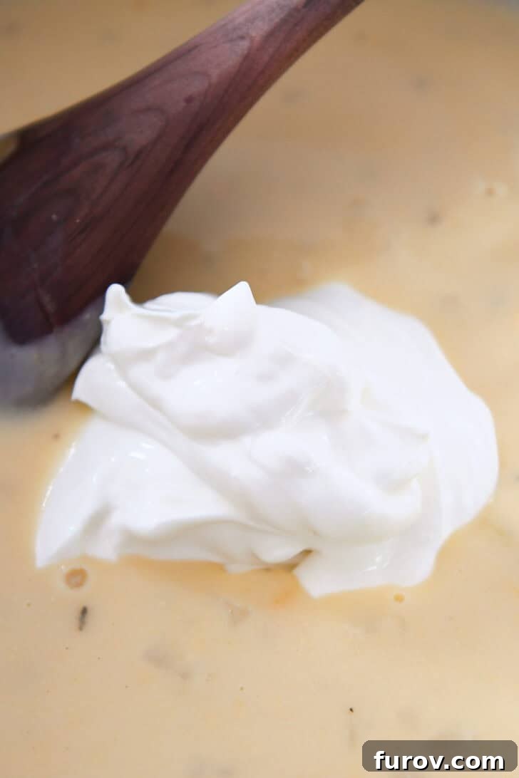 A large dollop of rich sour cream resting on a smooth, creamy sauce in a pot, adding a tangy finish.