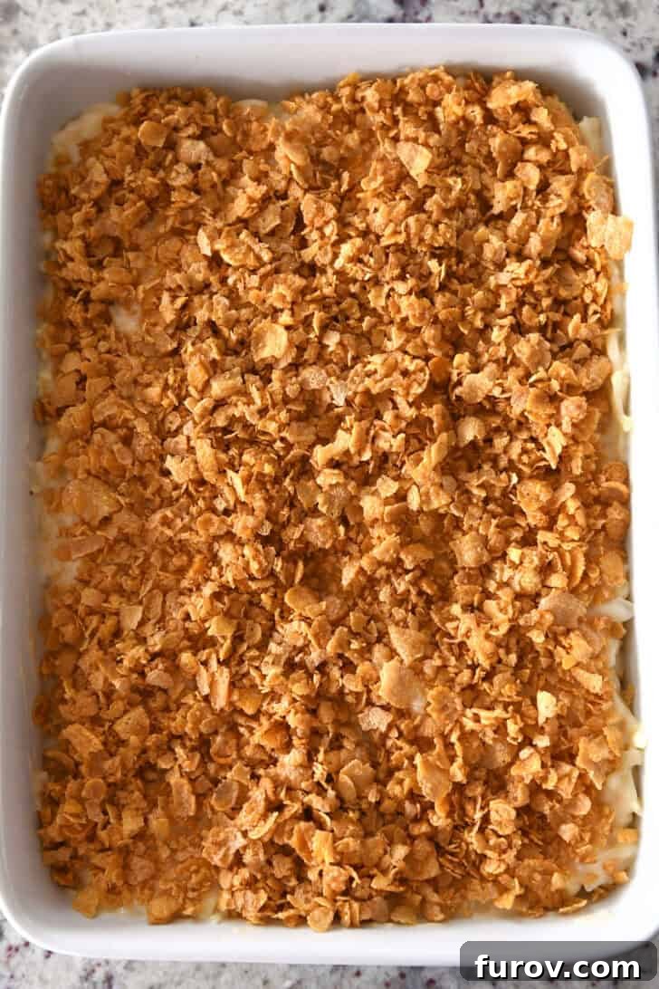 Top-down view of a baking dish filled with au gratin potatoes, beautifully topped with golden, crunchy cornflakes, ready for the oven.