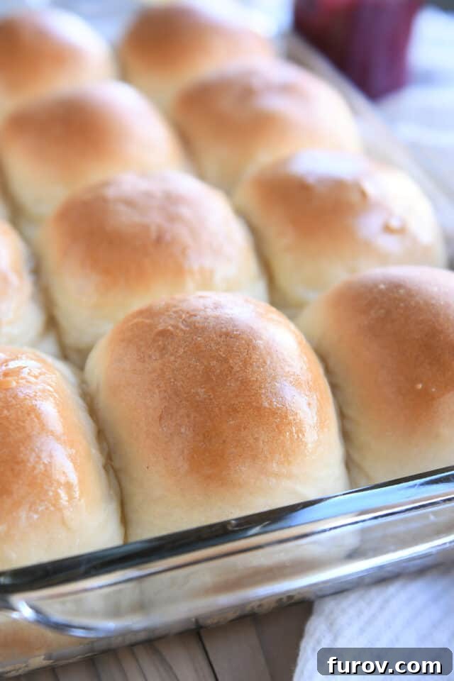 Golden-brown, buttered soft dinner rolls baked in a clear glass pan, ready to be served.