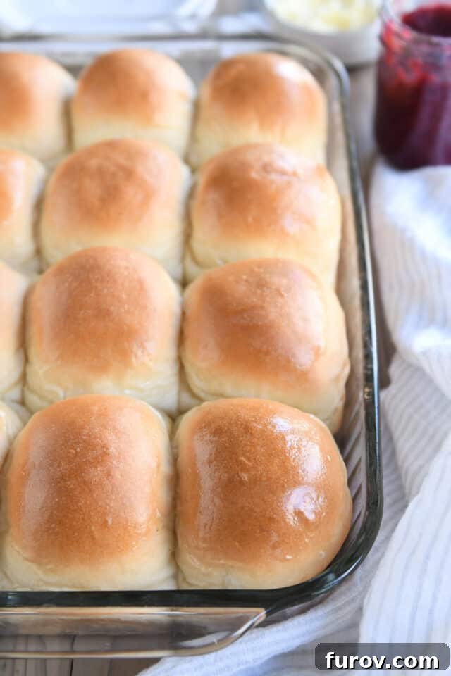 A glass baking pan filled with twelve freshly baked, golden-brown dinner rolls, glistening with melted butter on their tops.