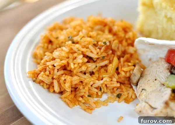 A white plate showcasing a scoop of Mexican rice next to a flavorful chicken fajita and a slice of golden cornbread.