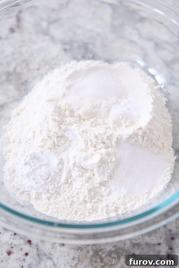 Dry ingredients like flour, baking powder, baking soda, and salt mixed in a clear glass bowl, ready for the wet ingredients.