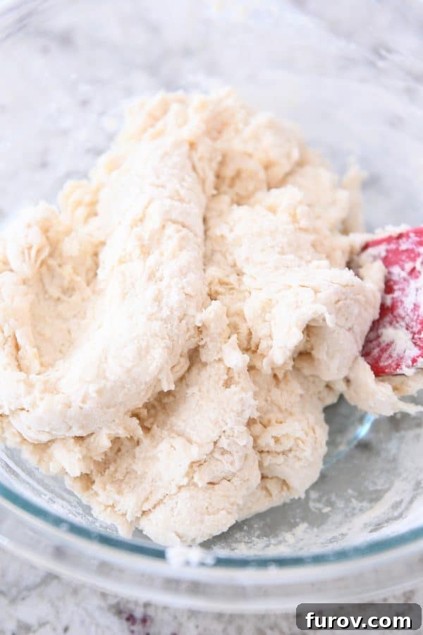 Close-up of biscuit dough being gently mixed with a spatula, showing its slightly lumpy texture.