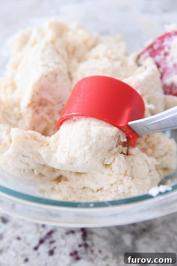 Scooping out sticky biscuit dough with a greased 1/4-cup measure, demonstrating the ease of portioning for drop biscuits.