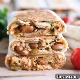 Three halves of crispy chicken enchilada wraps stacked on a wooden board with cherry tomatoes for garnish, highlighting their delicious appearance.