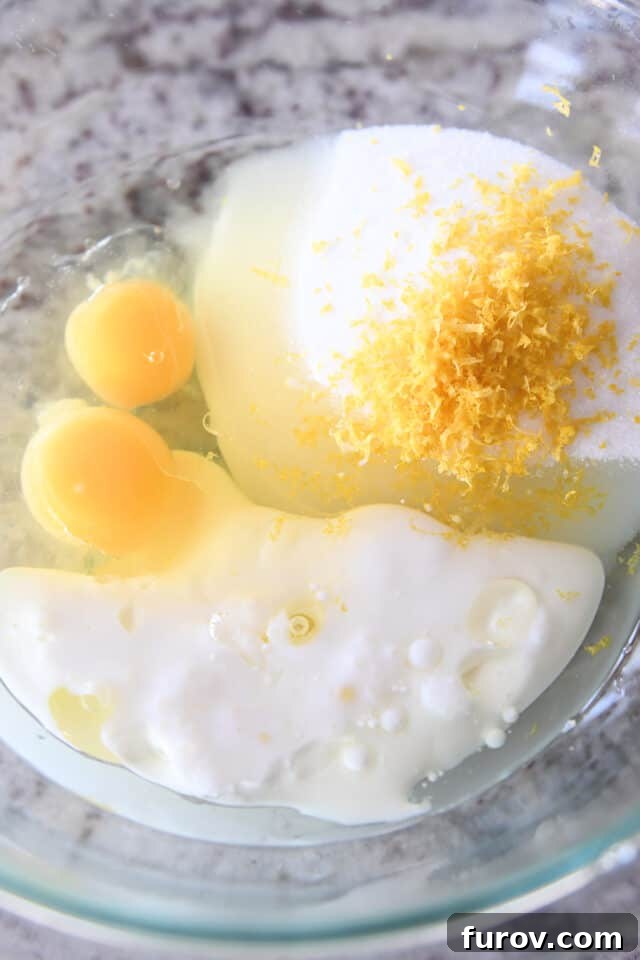 Glass bowl containing milk, eggs, lemon zest, and sugar, blended into a smooth wet mixture.