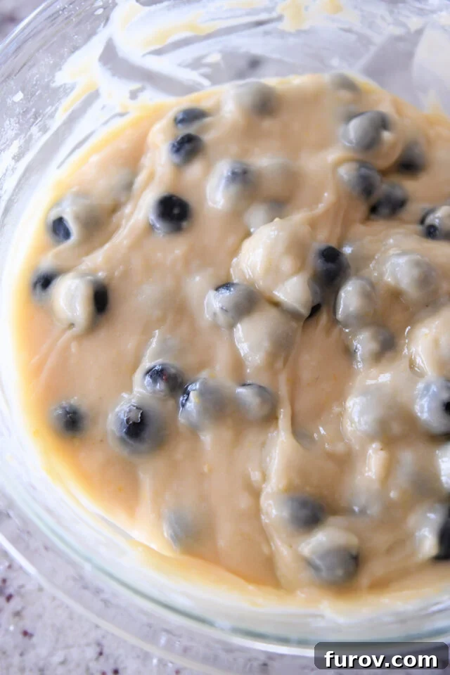 Smooth blueberry muffin batter in a glass bowl, speckled with perfectly folded-in blueberries.