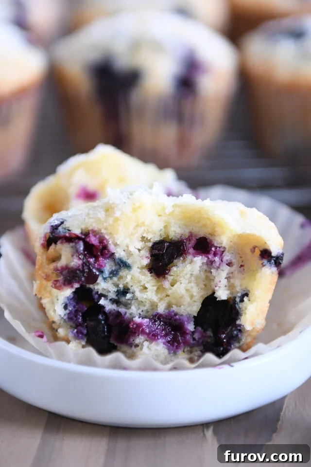 Half of a baked blueberry muffin, revealing its moist interior and generous blueberry distribution, served in a small white dish.