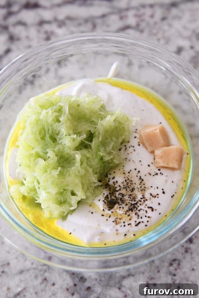 Ultimate Easy Chicken Gyros 5 Glass bowl filled with thick Greek yogurt, grated cucumber, minced garlic, and black pepper, ingredients for tzatziki.