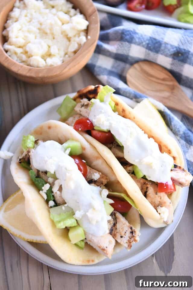 Ultimate Easy Chicken Gyros 6 Two beautifully assembled chicken gyros with fresh toppings on a plate, garnished with lemon slices.