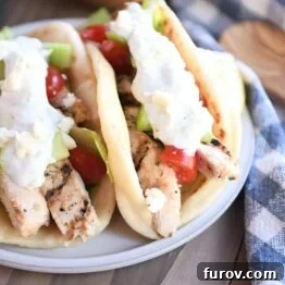 Two chicken gyros in flatbread with tzatziki, tomatoes and lettuce on gray plate.
