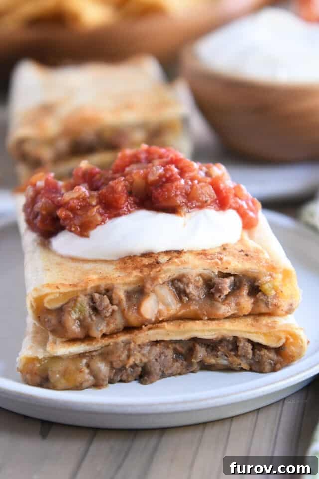Two halves of crispy beef and bean wraps on a gray plate, garnished with fresh salsa and a dollop of sour cream.
