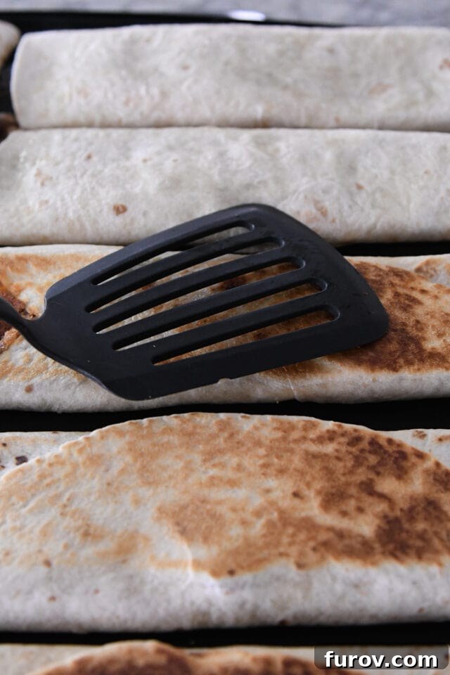 A spatula pressing down on a beef and bean tortilla wrap on a hot griddle, creating a perfectly crispy exterior.