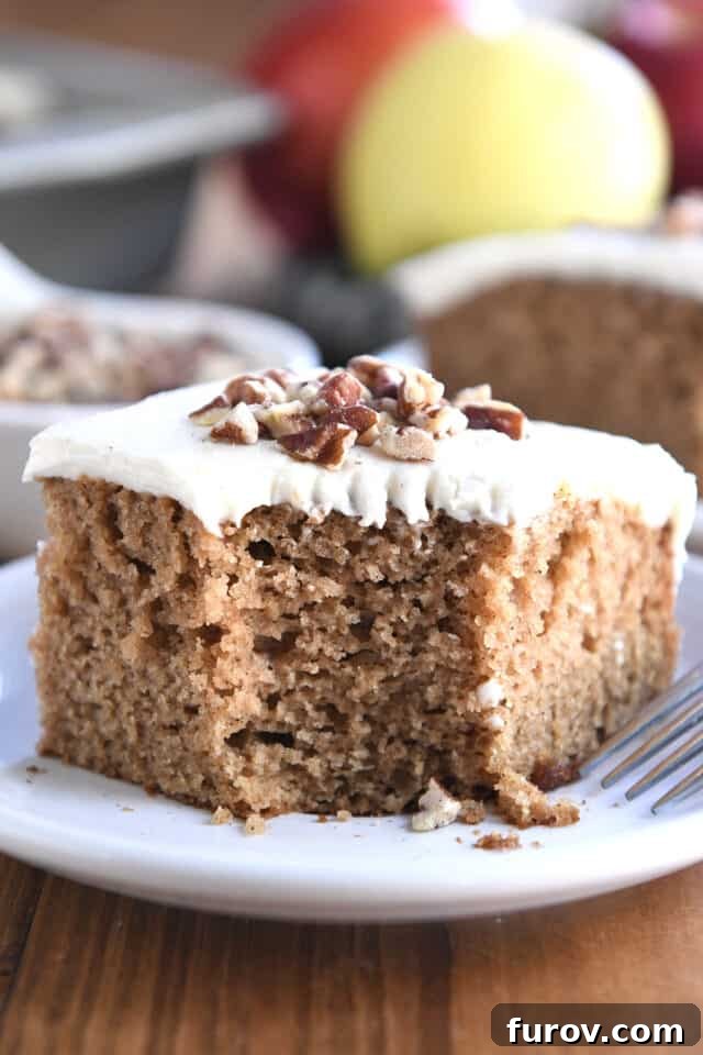 Spiced Apple Comfort Cake with Brown Butter Cream Cheese Swirl 2 Square of frosted applesauce spice cake on white plate with pecans on top.