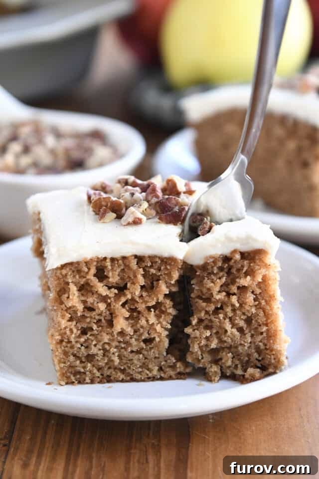 Spiced Apple Comfort Cake with Brown Butter Cream Cheese Swirl 11 Fork taking bite of frosted applesauce spice cake on white plate.