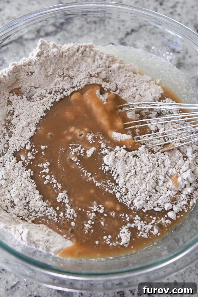 Spiced Apple Comfort Cake with Brown Butter Cream Cheese Swirl 5 Glass bowl with whisk mixing dry ingredients into wet ingredients for applesauce spice cake.