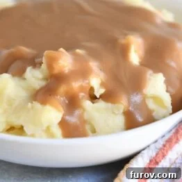 White bowl with mashed potatoes and brown gravy.