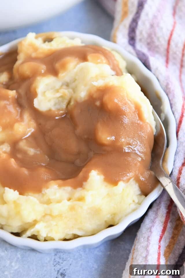 White dish with mashed potatoes, brown gravy and spoon.