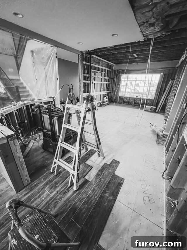 A black and white photograph showcasing the initial demolition phase of a kitchen remodel, with exposed framing and removed cabinetry.