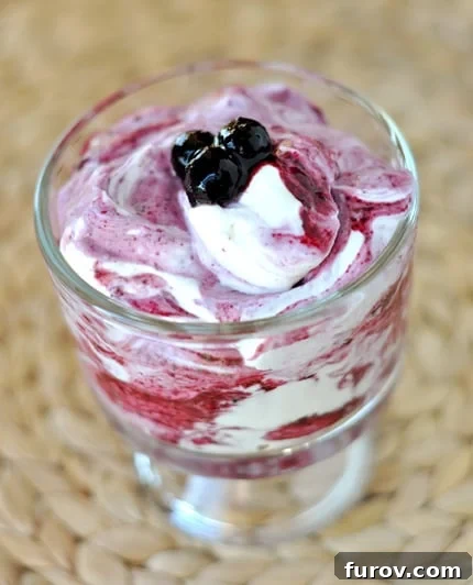 A glass goblet with a blueberry and yogurt mixture topped with a few blueberries.