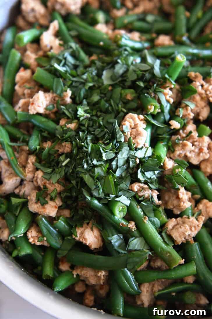 20-Minute Thai Turkey & Green Bean Dinner 5 Fragrant fresh Thai basil leaves being added to the sizzling ground turkey and green beans in a stainless steel skillet, infusing the dish with its signature aroma.