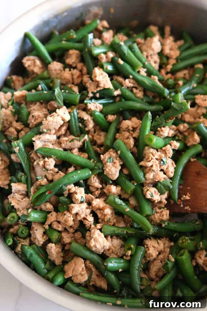20-Minute Thai Turkey & Green Bean Dinner 6 A top-down view of the ground turkey, vibrant green beans, and aromatic seasonings perfectly stirred together in a gleaming stainless steel skillet, showcasing the rich colors of the Thai-style dish.