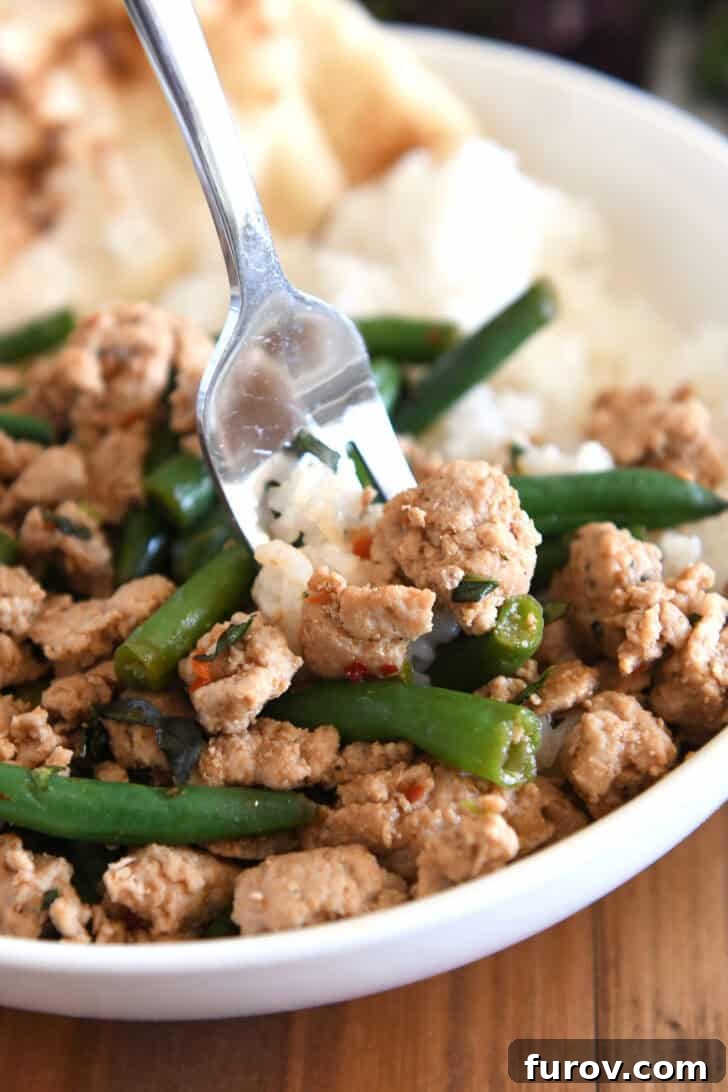 20-Minute Thai Turkey & Green Bean Dinner 8 A fork lifts a savory bite of rice, ground turkey, and green beans from a white bowl, highlighting the delicious textures and colors of the Thai-style dish.