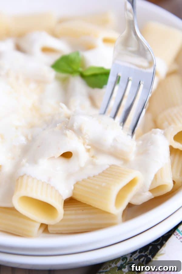 A fork lifts a bite of creamy homemade Alfredo sauce over rigatoni noodles, showcasing the rich texture and inviting warmth of the dish.