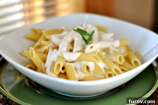 A beautifully composed white bowl of pasta generously drizzled with rich, creamy Alfredo sauce, ready to be enjoyed.