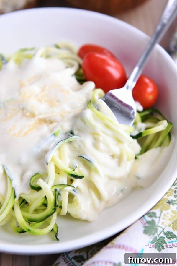 A close-up shot of creamy homemade Alfredo sauce coating zoodles in a white bowl, emphasizing the appealing texture and healthy twist.