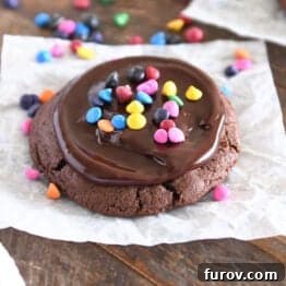 One chocolate cookie spread with chocolate ganache and sprinkled with rainbow chips on white parchment paper.