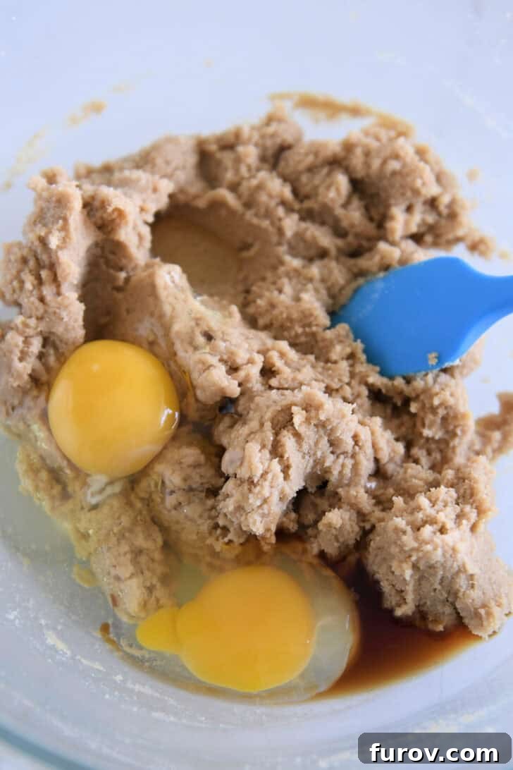 Glass bowl with two eggs and brown sugar cookie dough with blue spatula.