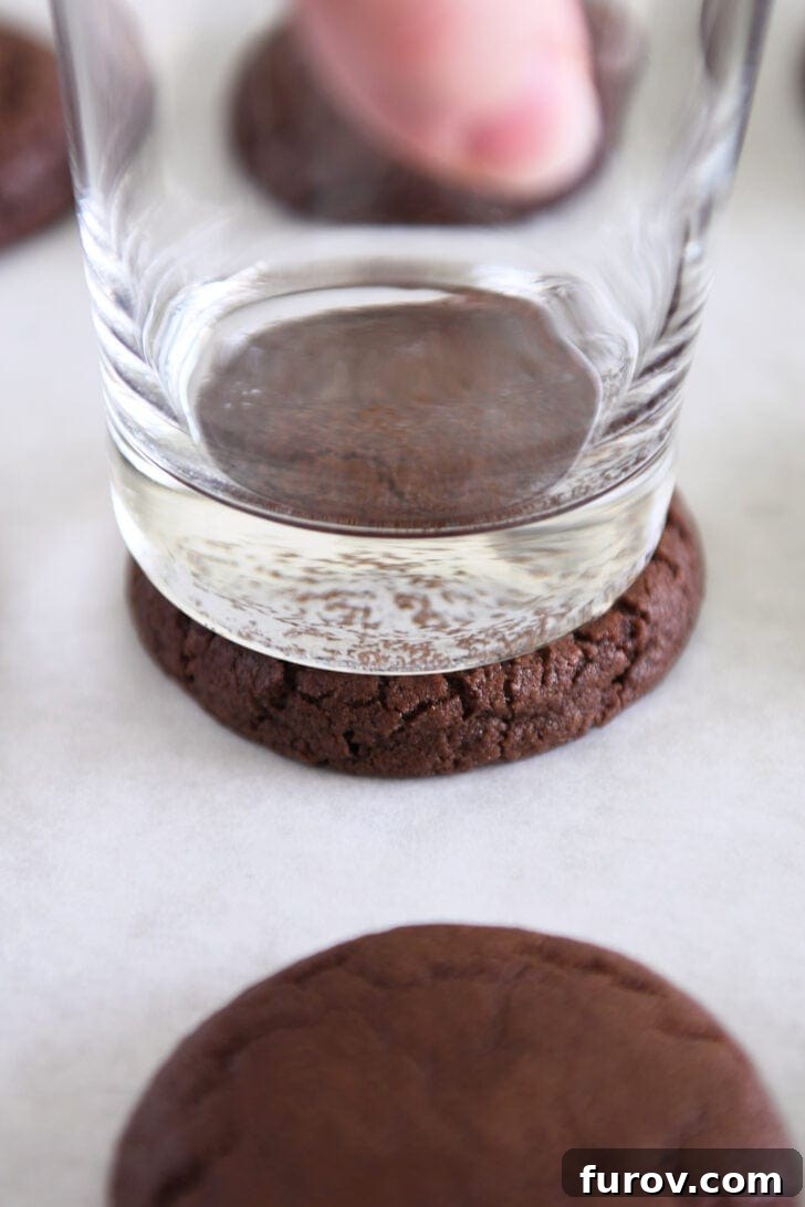 Pressing chocolate cookie to an even thickness with flat bottomed glass.