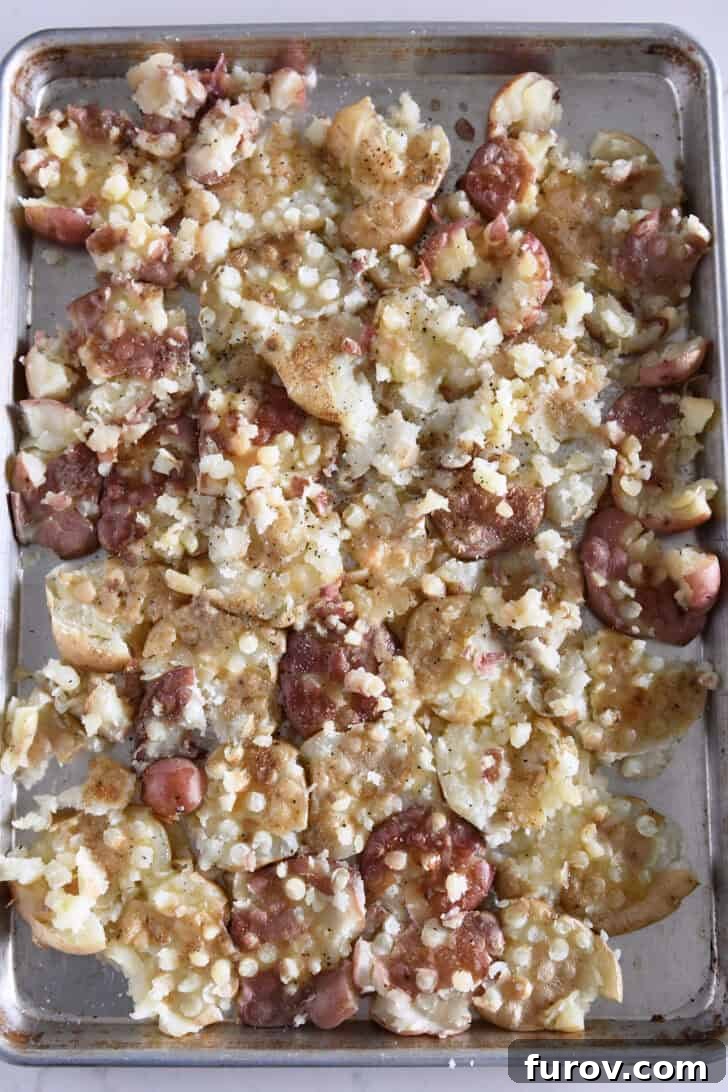 Top down view of smashed potatoes drizzled with butter and salt and pepper on half sheet pan.