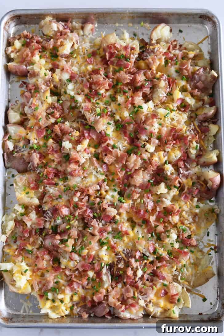 Top down view of cheesy garlic smashed potatoes topped with chives on half sheet pan.