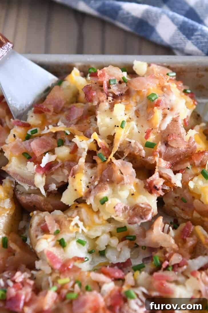 Square spatula scooping portion of cheesy smashed potatoes off of half sheet pan.