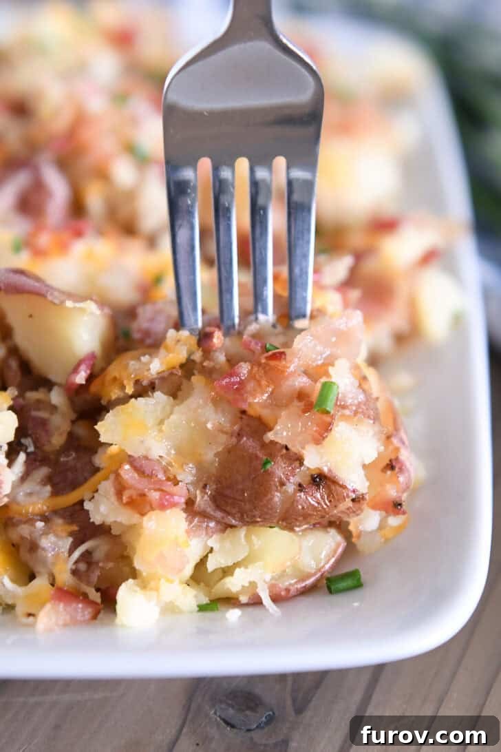 Fork piercing bite of cheesy smashed potatoes on white tray.