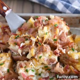 Spatula scooping serving of cheesy smashed potatoes off of half sheet pan.