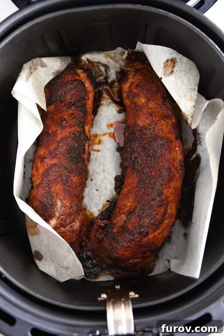 Speedy and Succulent Air Fryer Pork Tenderloin 6 Two golden-brown pork tenderloins cooking in an air fryer on parchment paper, midway through the cooking process.